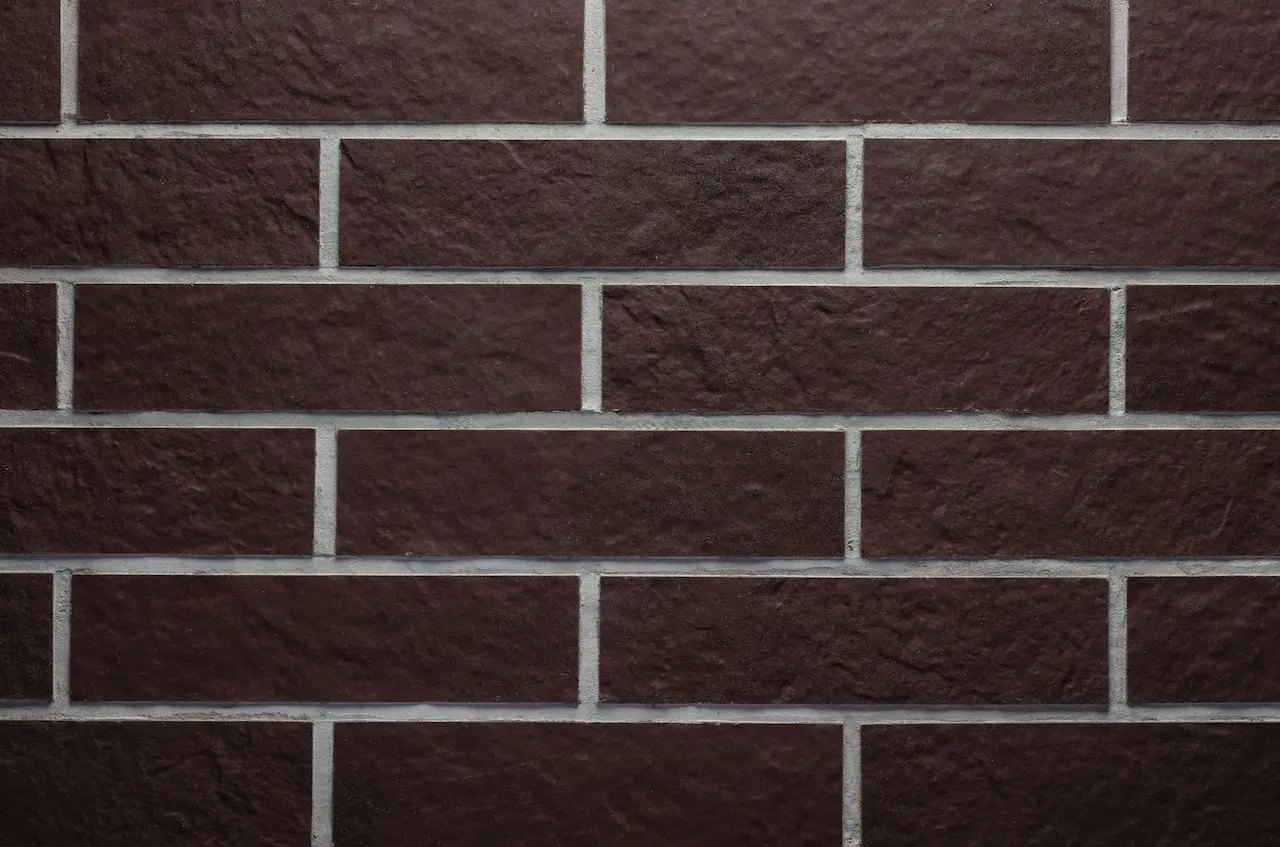 Chocolate-brown masonry BR07 Chocolate Rock with light-gray joints and a rough stone texture