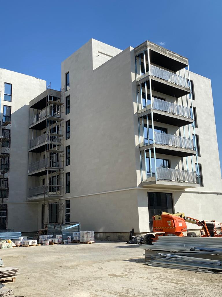 End of a block with stacked balconies in beige flexible stone, next to an orange lift platform