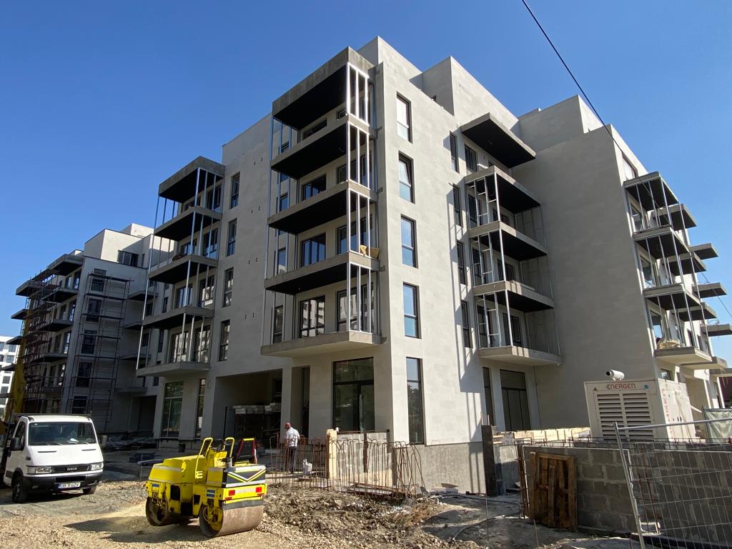 Blocks with balconies in beige flexible stone, a road roller and a truck in front