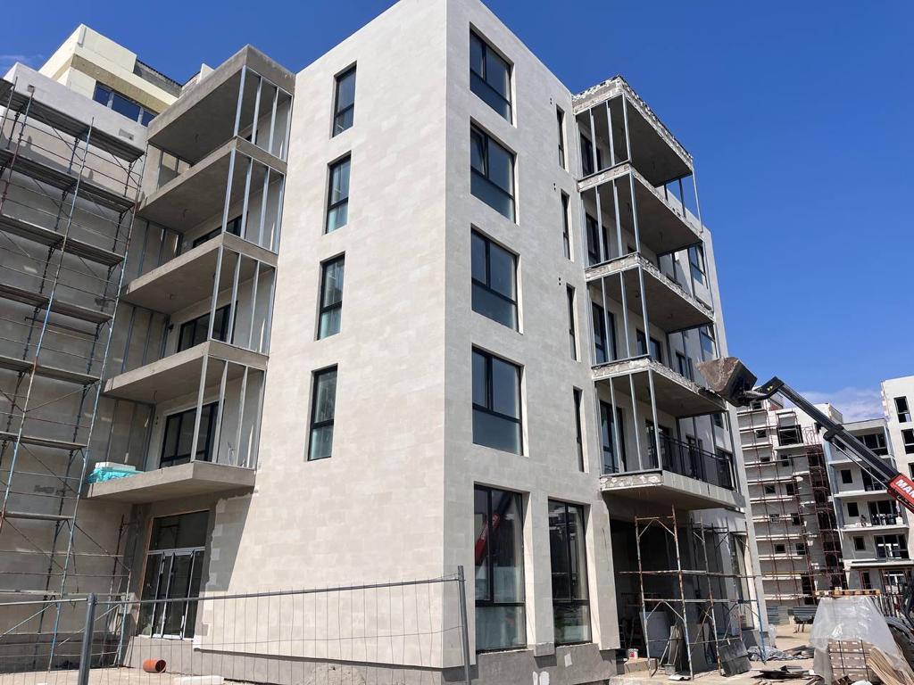 Contemporary block under construction, clad in large-format flexible stone, with cantilevered balconies