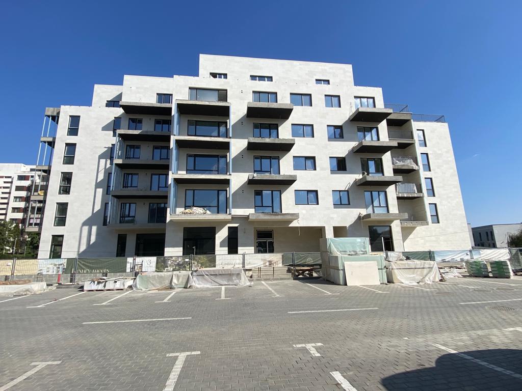 Main facade of an apartment block in light flexible stone, with stacked balconies and a car park