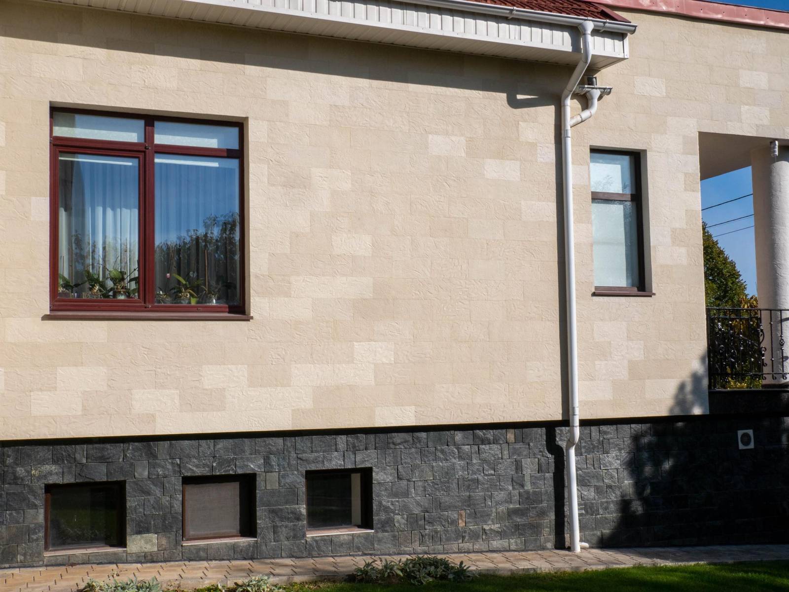 Corner of the house with a window, white downpipe and Tender Rock flexible stone, from below
