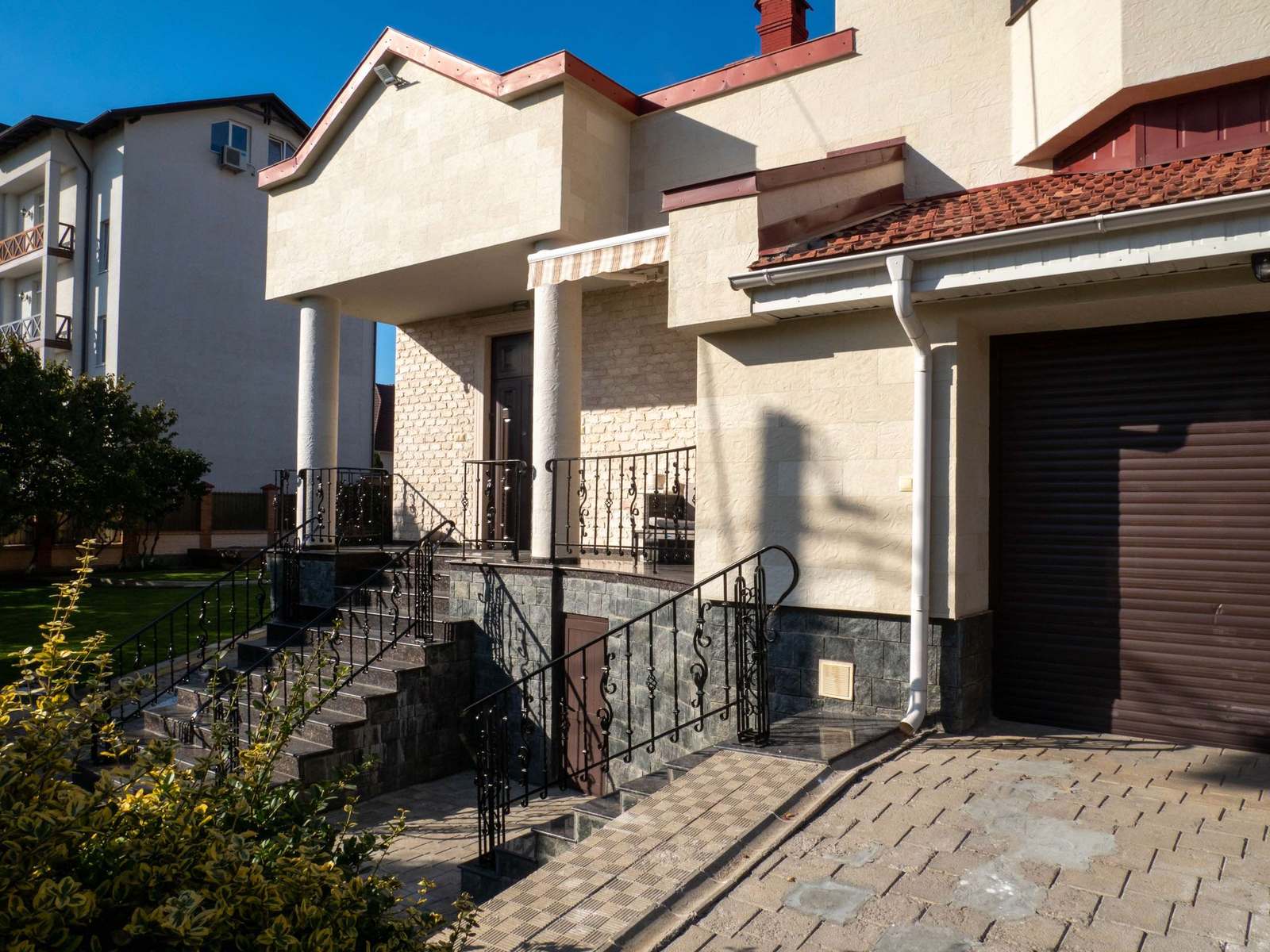 Street facade with two brown garage doors, steps and wrought-iron railings