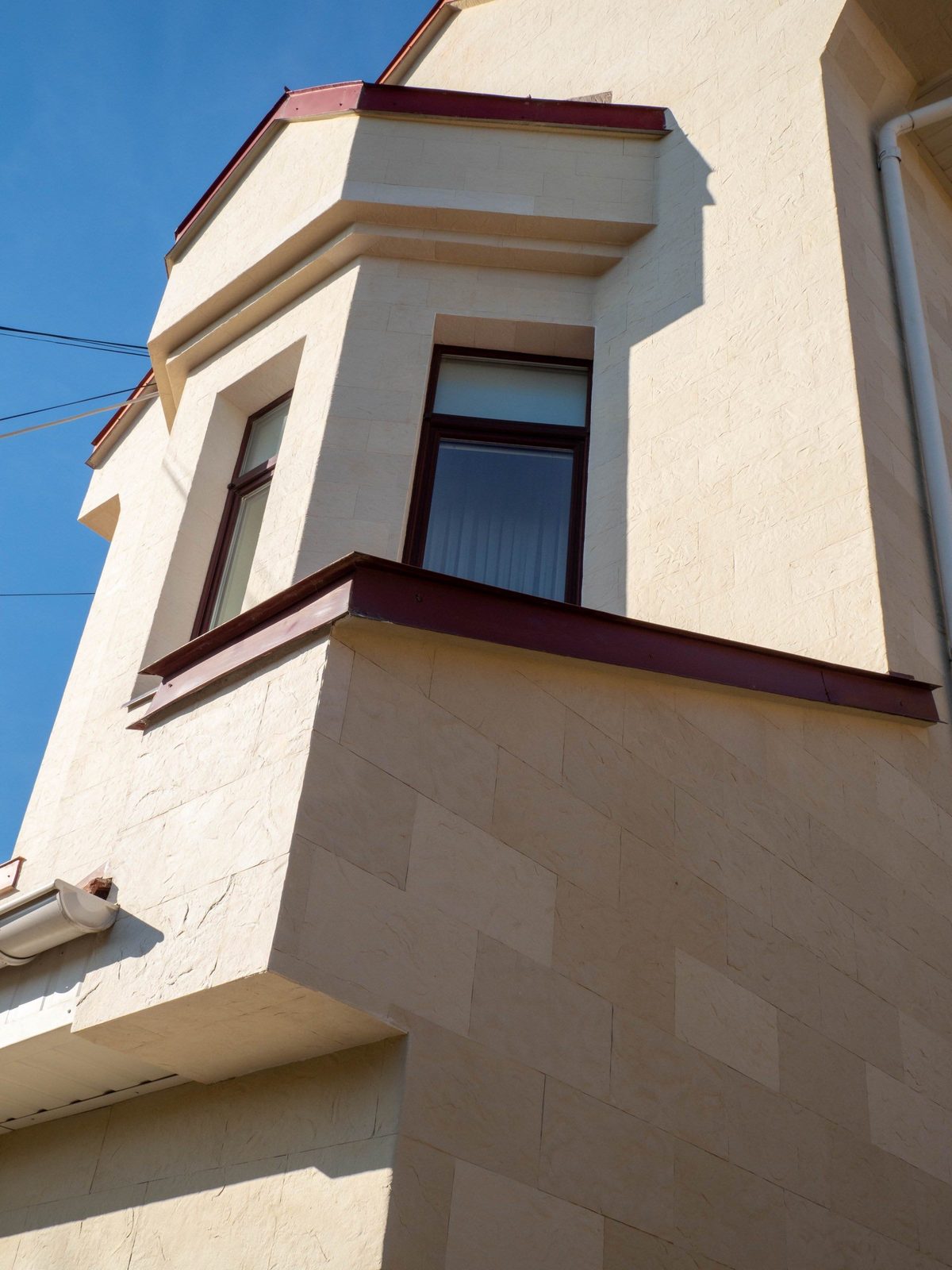 Tall gable and bay window seen from below, beige flexible stone and brown window frames