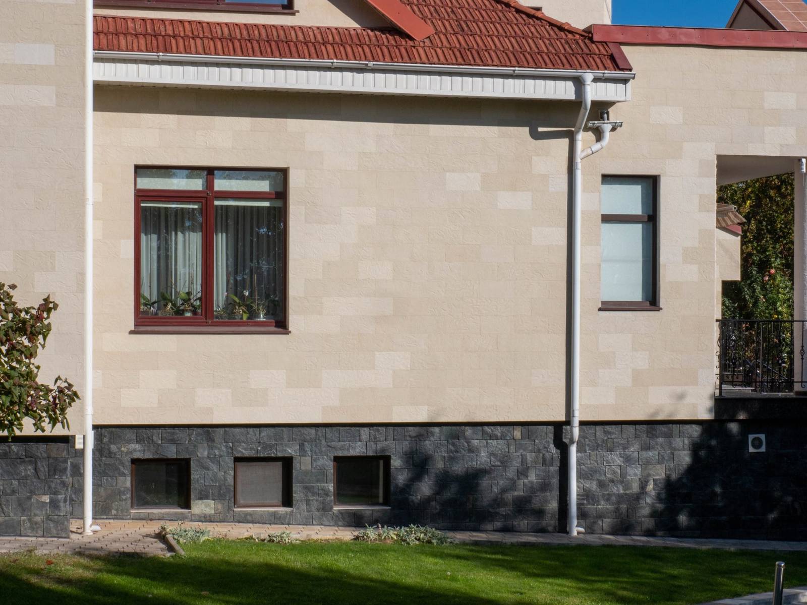 Side view of the house with large windows and a red roof, clad in beige flexible stone