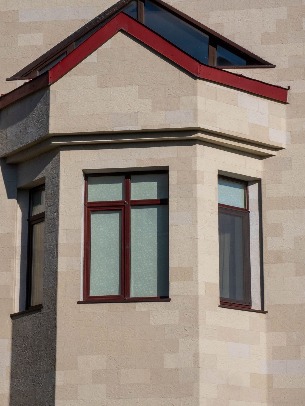 Bay window with its own tiled roof, clad in Tender Rock flexible stone, against a blue sky