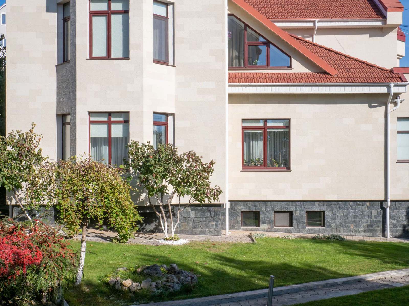 Side of the house with brown-framed windows and a Tender Rock flexible stone facade, shrubs in front