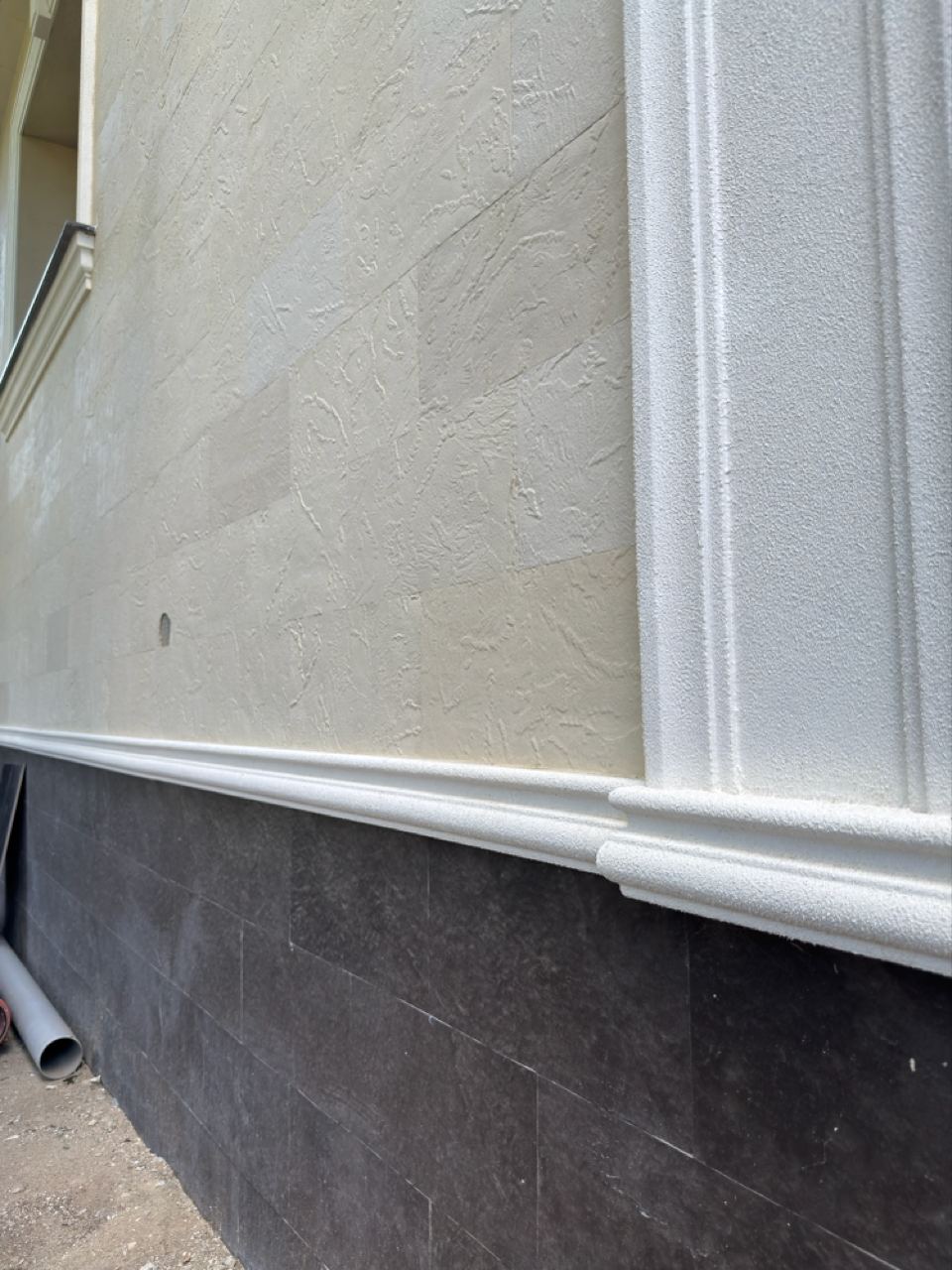 Line of the dark plinth under the light flexible stone wall, next to a downpipe