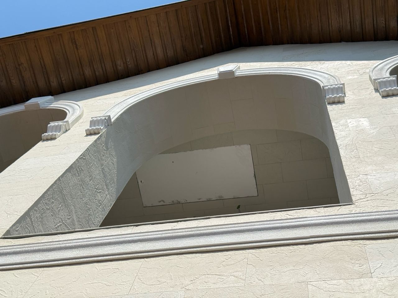 Arched balcony with white rustication on the light flexible stone facade