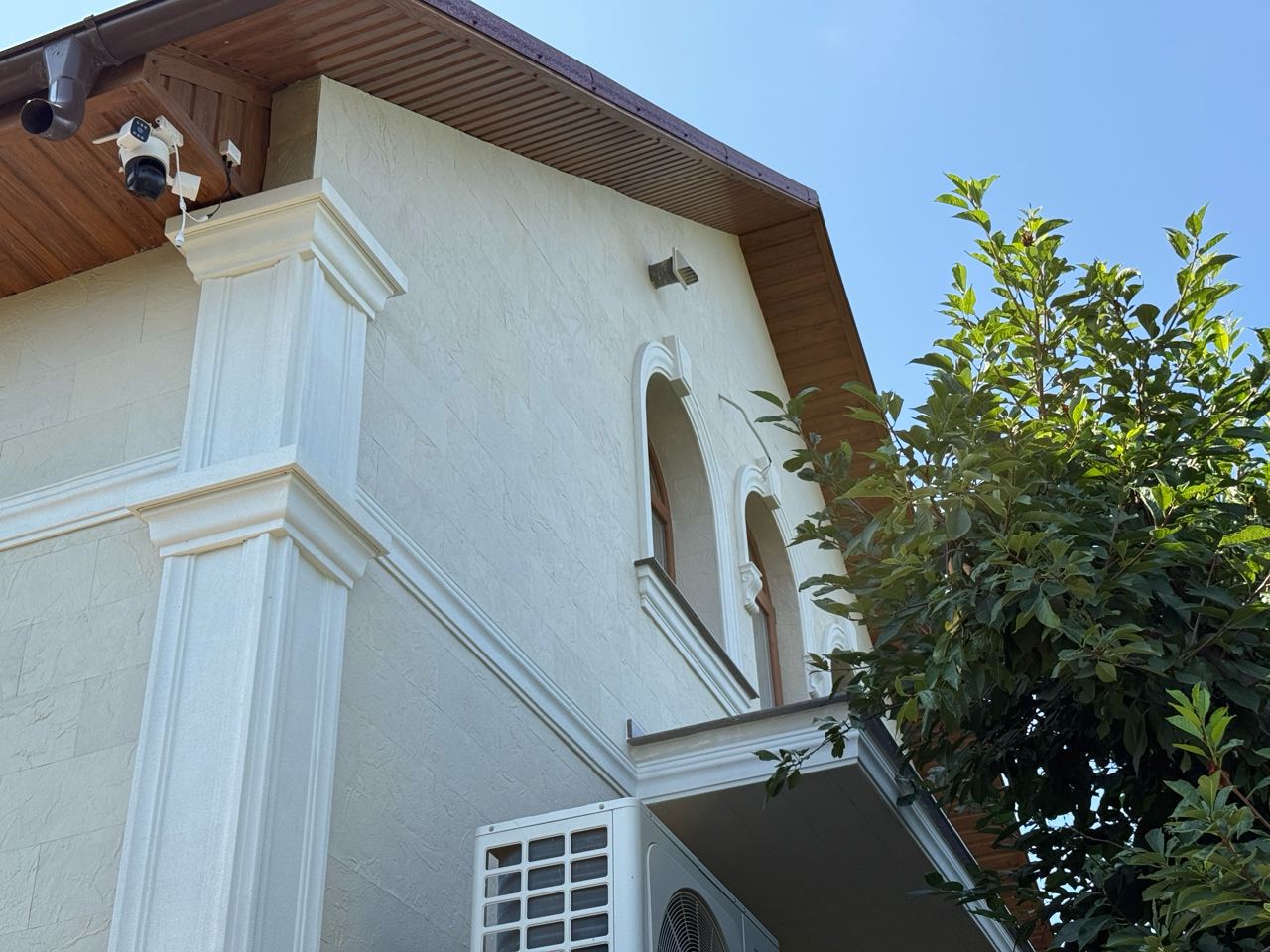 Facade from below: white pilaster, arched window and light flexible stone under the eaves
