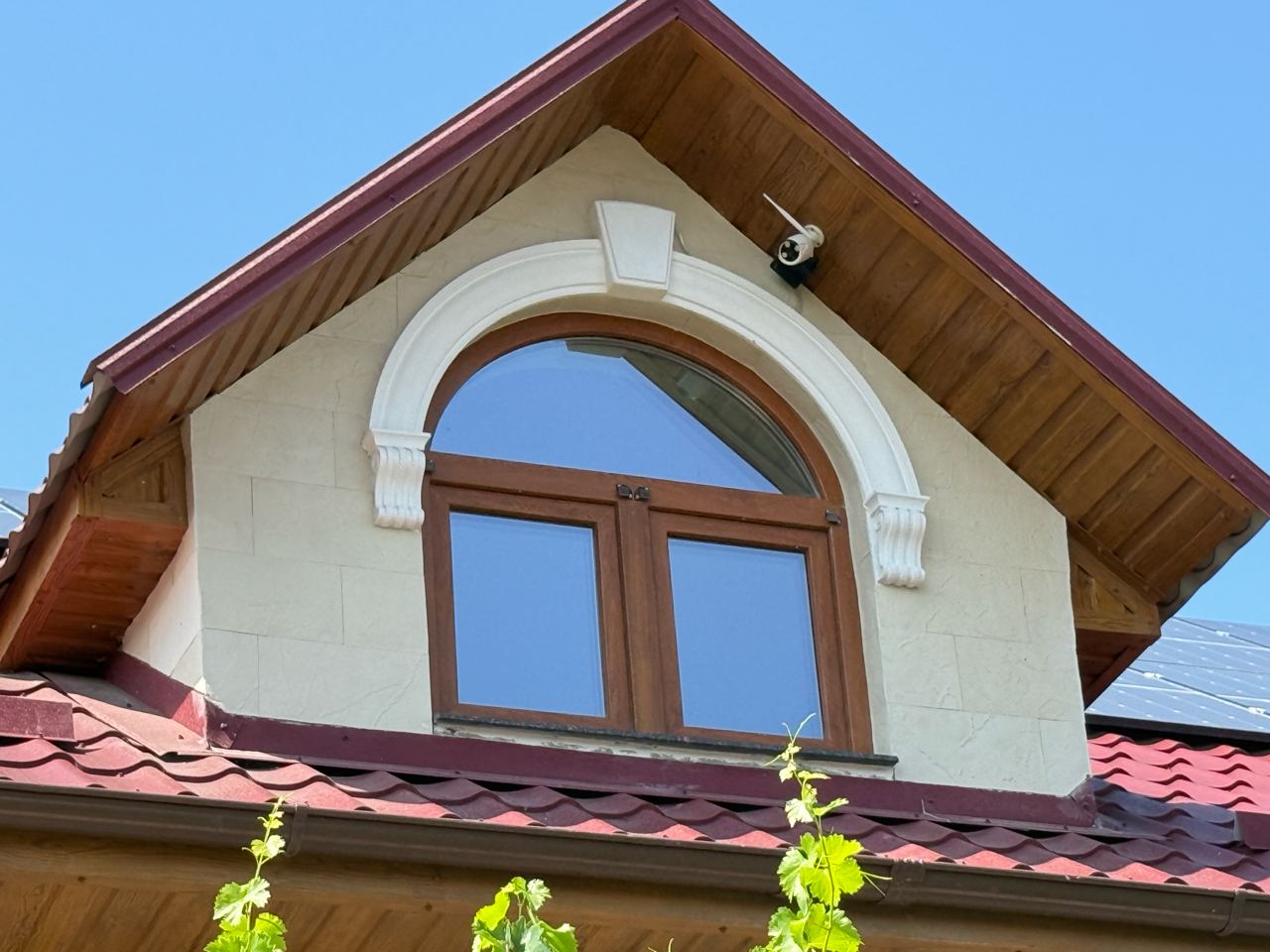 Dormer with an arched window and white surround, light flexible stone under the red roof