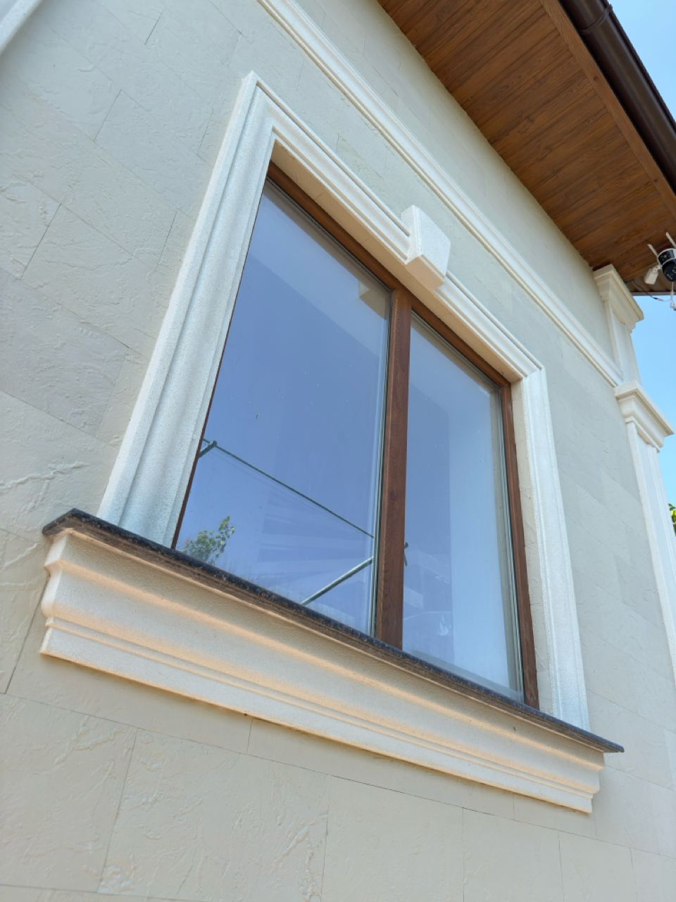 Window with a white surround and wooden frame, cornice under the eaves, light flexible stone