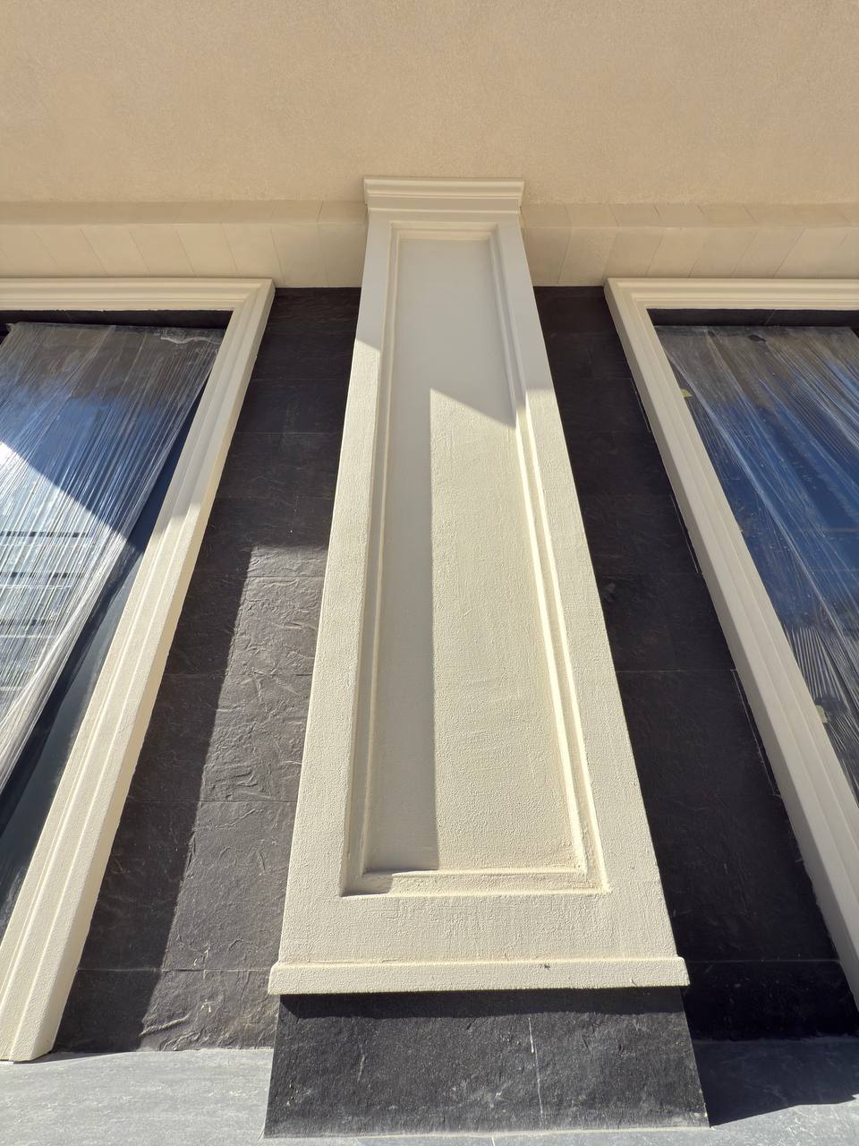 Beige fluted pilaster on a vertical anthracite panel between two windows, seen from below