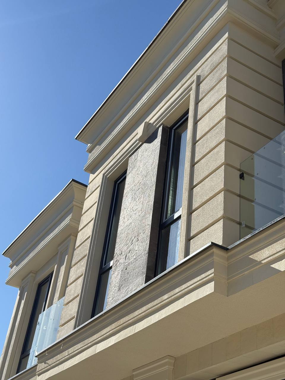 Corner with fluted pilasters and a beige cornice, anthracite vertical panel beside a window, from below