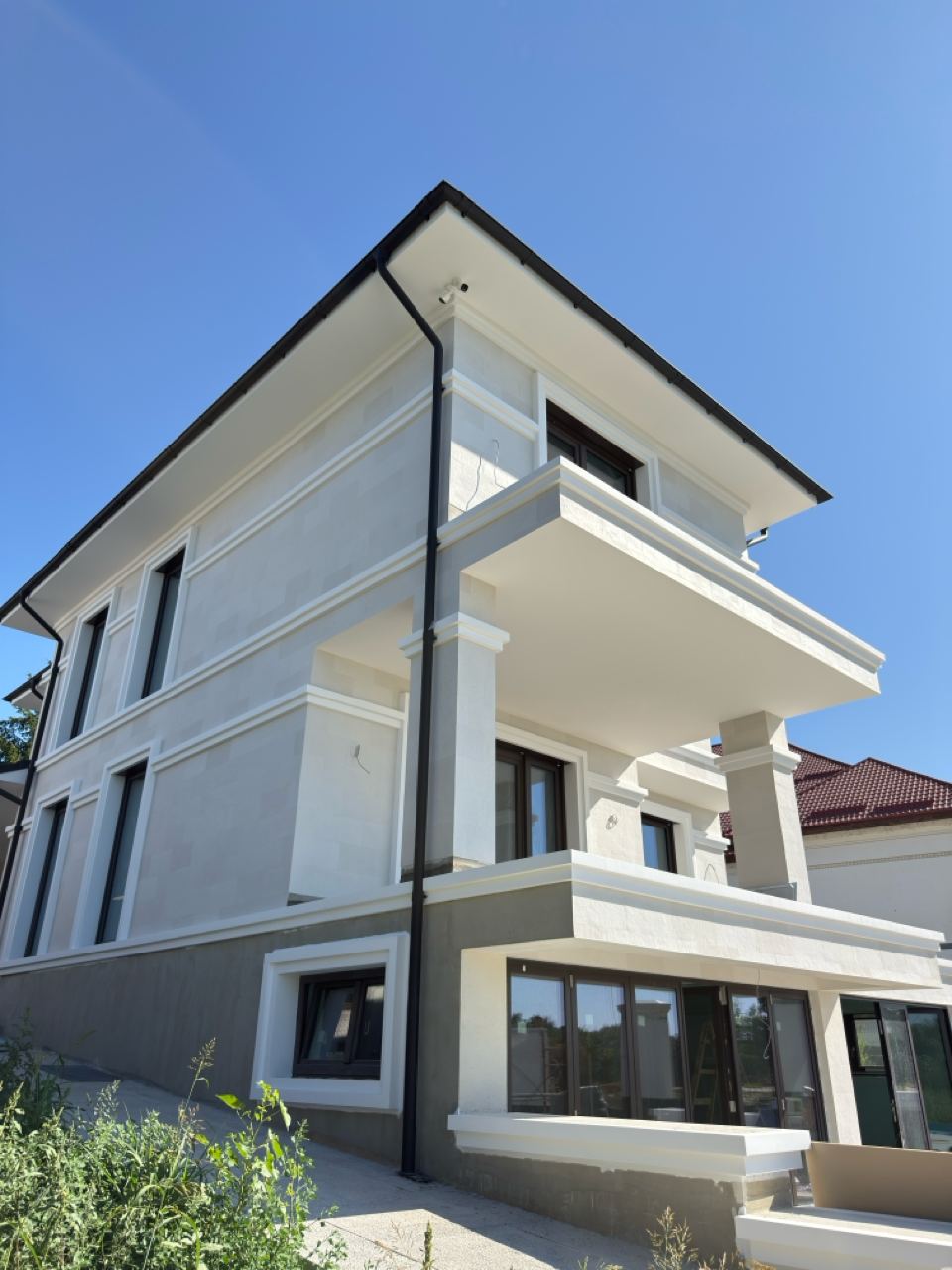 The whole house from the street, three storeys in white flexible stone with white cornices, plants in front